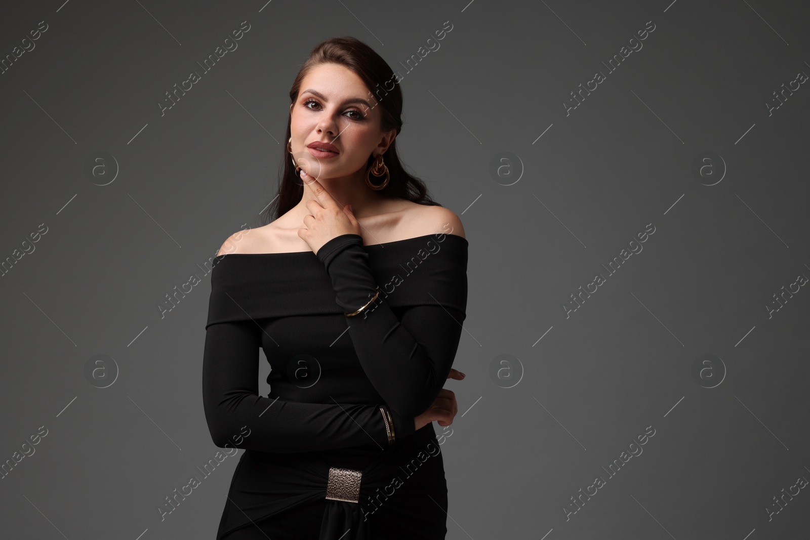 Young woman in stylish black dress on grey background Photo of Young woman in stylish black dress on grey background