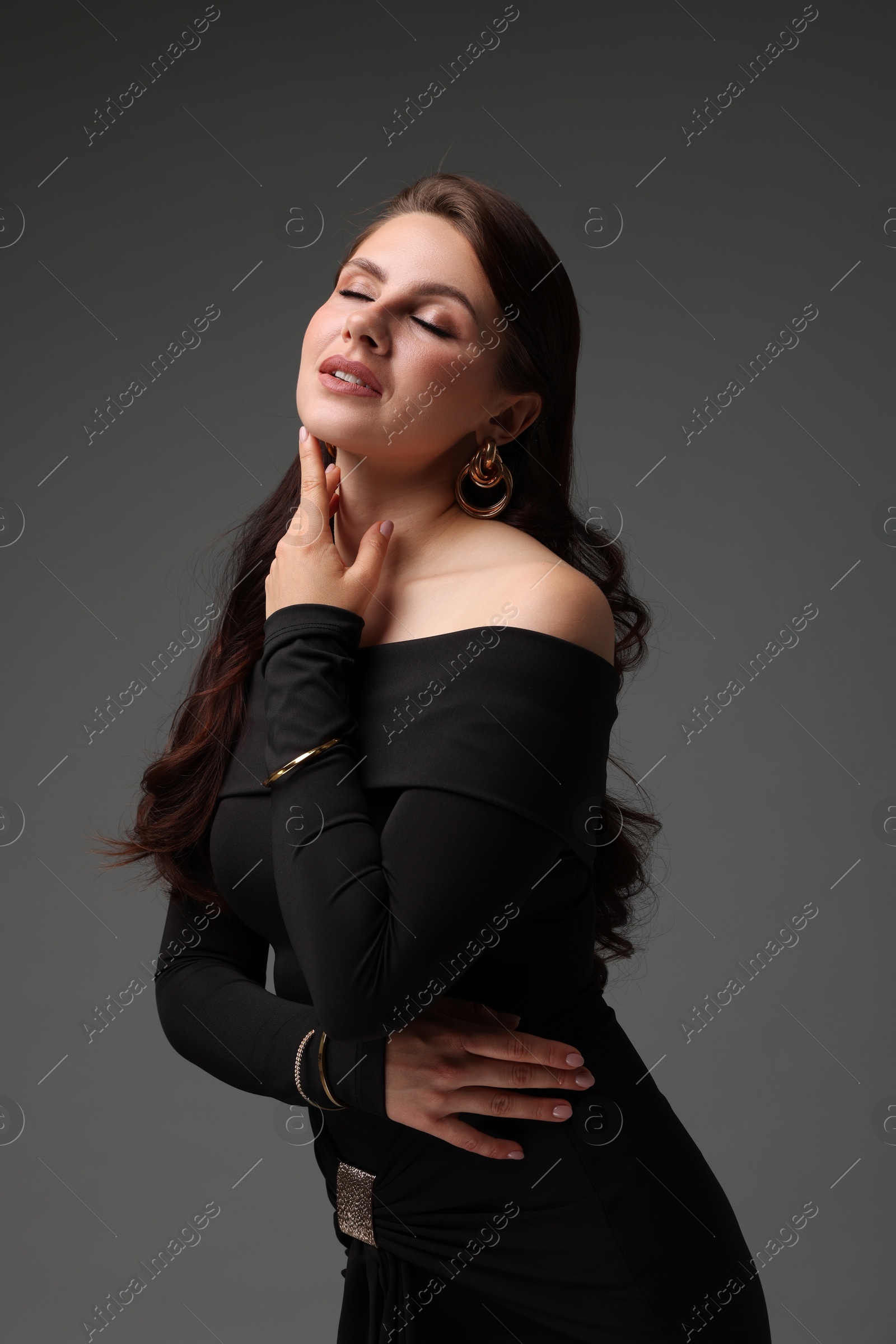 Young woman in stylish black dress on grey background Photo of Young woman in stylish black dress on grey background