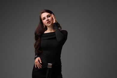 Photo of Young woman in stylish black dress on grey background, space for text