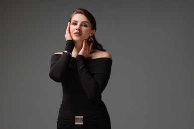 Photo of Young woman in stylish black dress on grey background, space for text