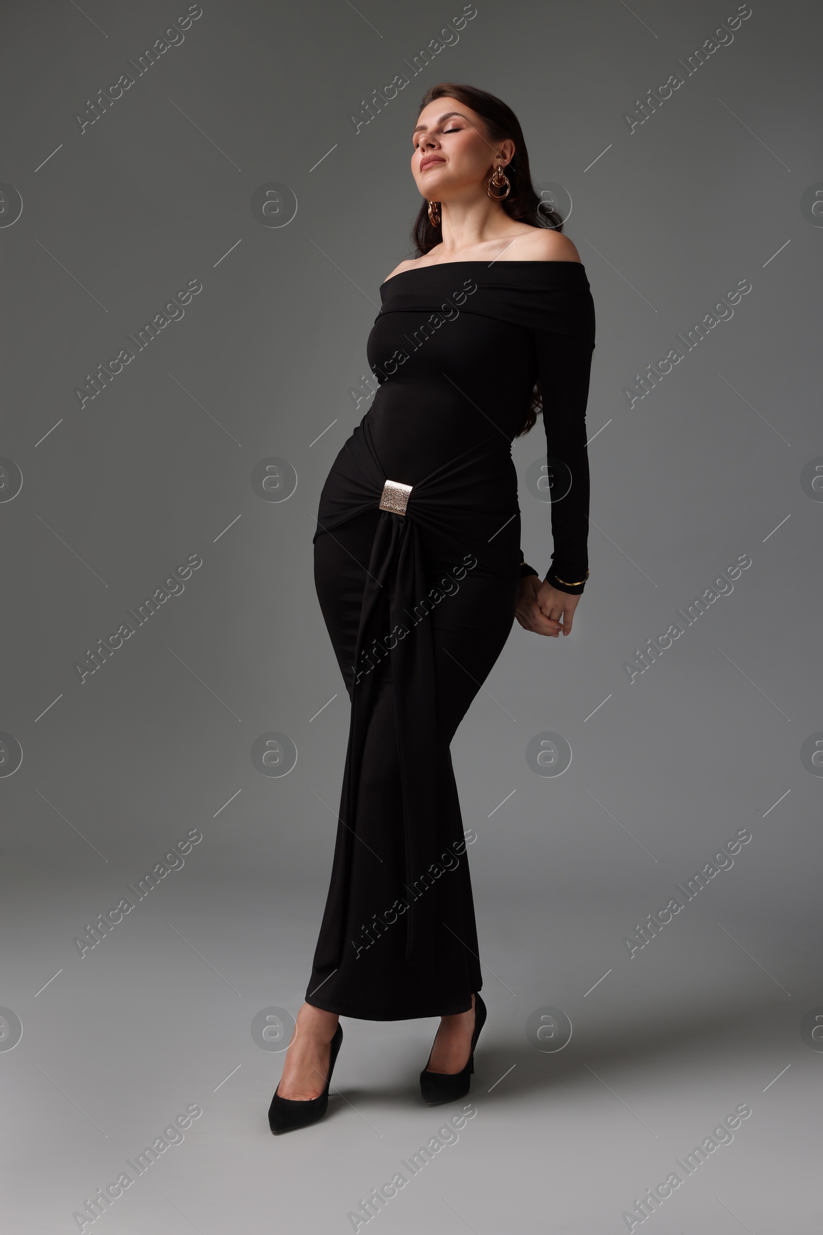 Young woman in stylish black dress on grey background Photo of Young woman in stylish black dress on grey background