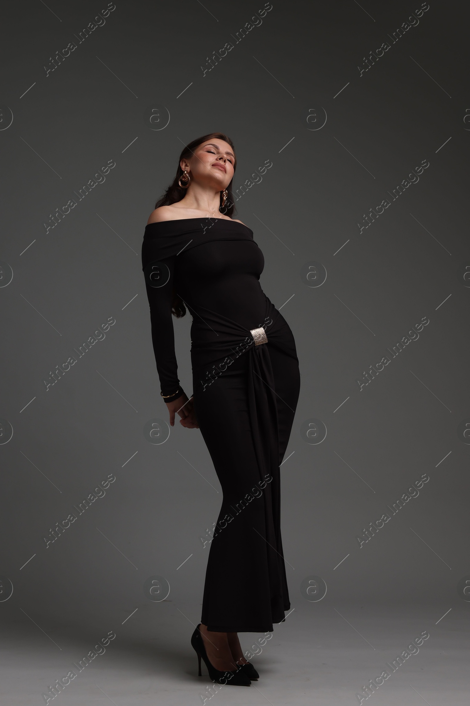 Young woman in stylish black dress on grey background Photo of Young woman in stylish black dress on grey background