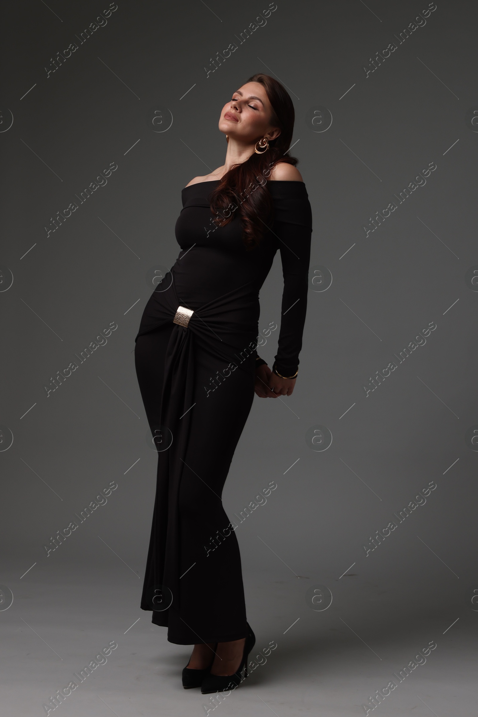 Young woman in stylish black dress on grey background Photo of Young woman in stylish black dress on grey background