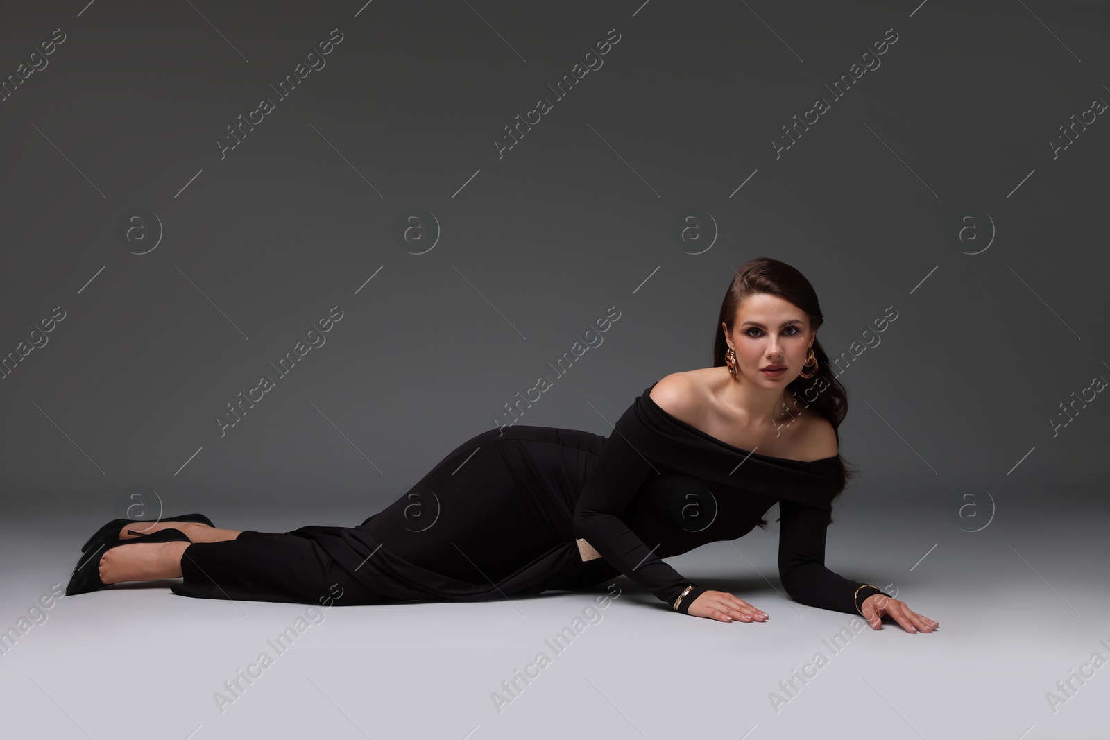Young woman in stylish black dress on grey background Photo of Young woman in stylish black dress on grey background