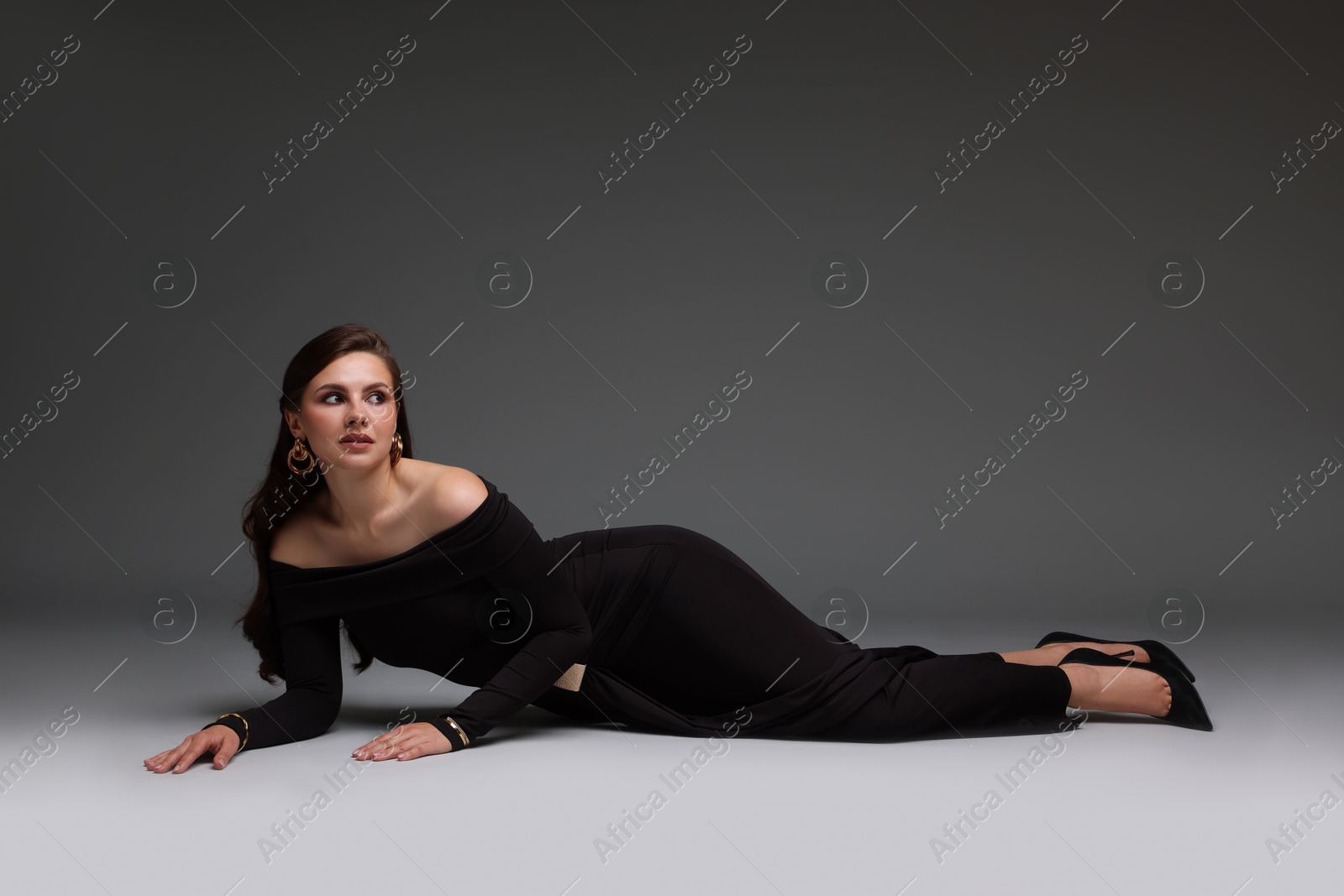 Young woman in stylish black dress on grey background Photo of Young woman in stylish black dress on grey background