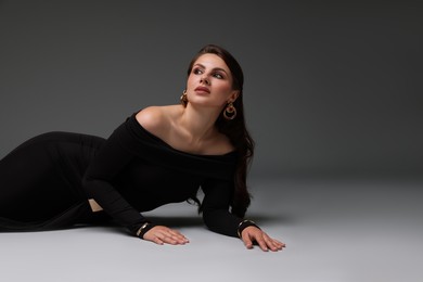 Photo of Young woman in stylish black dress on grey background, space for text