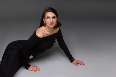Photo of Young woman in stylish black dress on grey background, space for text