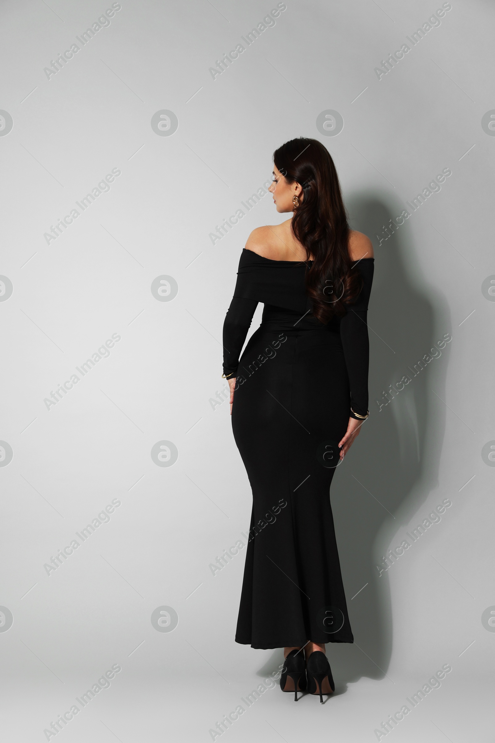Young woman in stylish black dress on light grey background, back view Photo of Young woman in stylish black dress on light grey background, back view