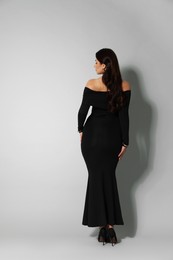 Photo of Young woman in stylish black dress on light grey background, back view