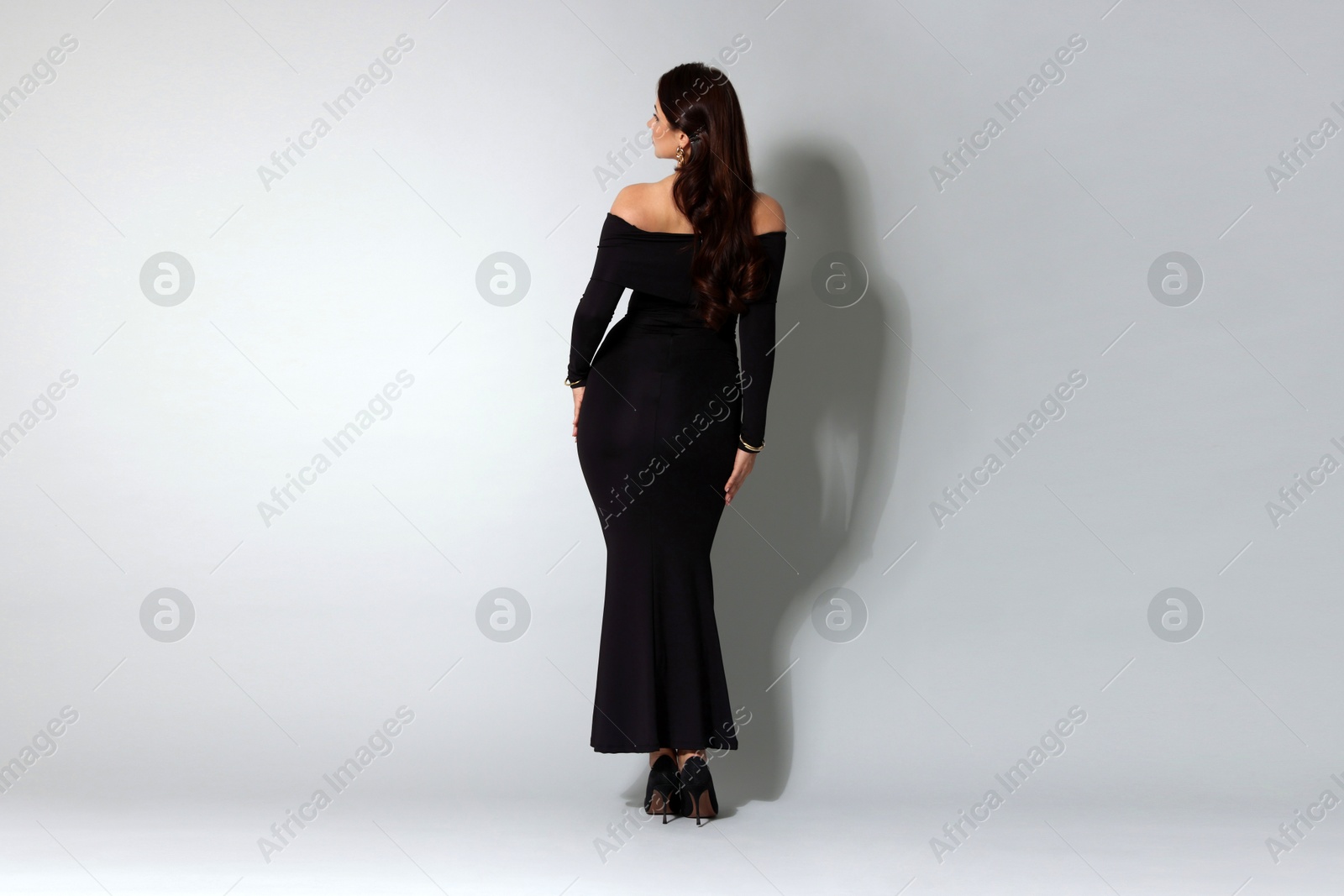 Young woman in stylish black dress on light grey background, back view Photo of Young woman in stylish black dress on light grey background, back view
