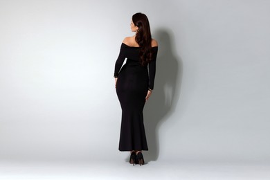 Photo of Young woman in stylish black dress on light grey background, back view