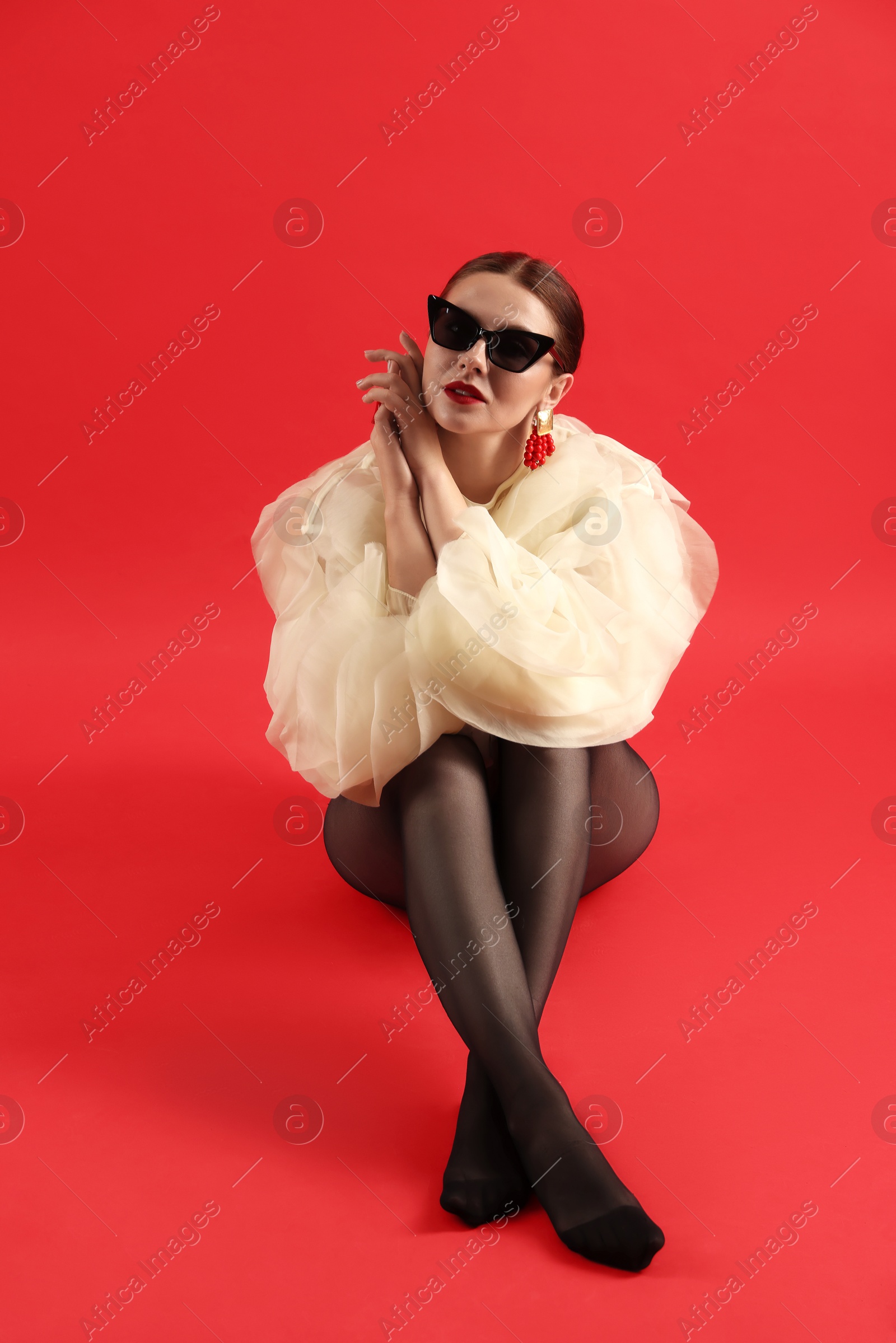Young woman in stylish clothes and sunglasses on red background Photo of Young woman in stylish clothes and sunglasses on red background