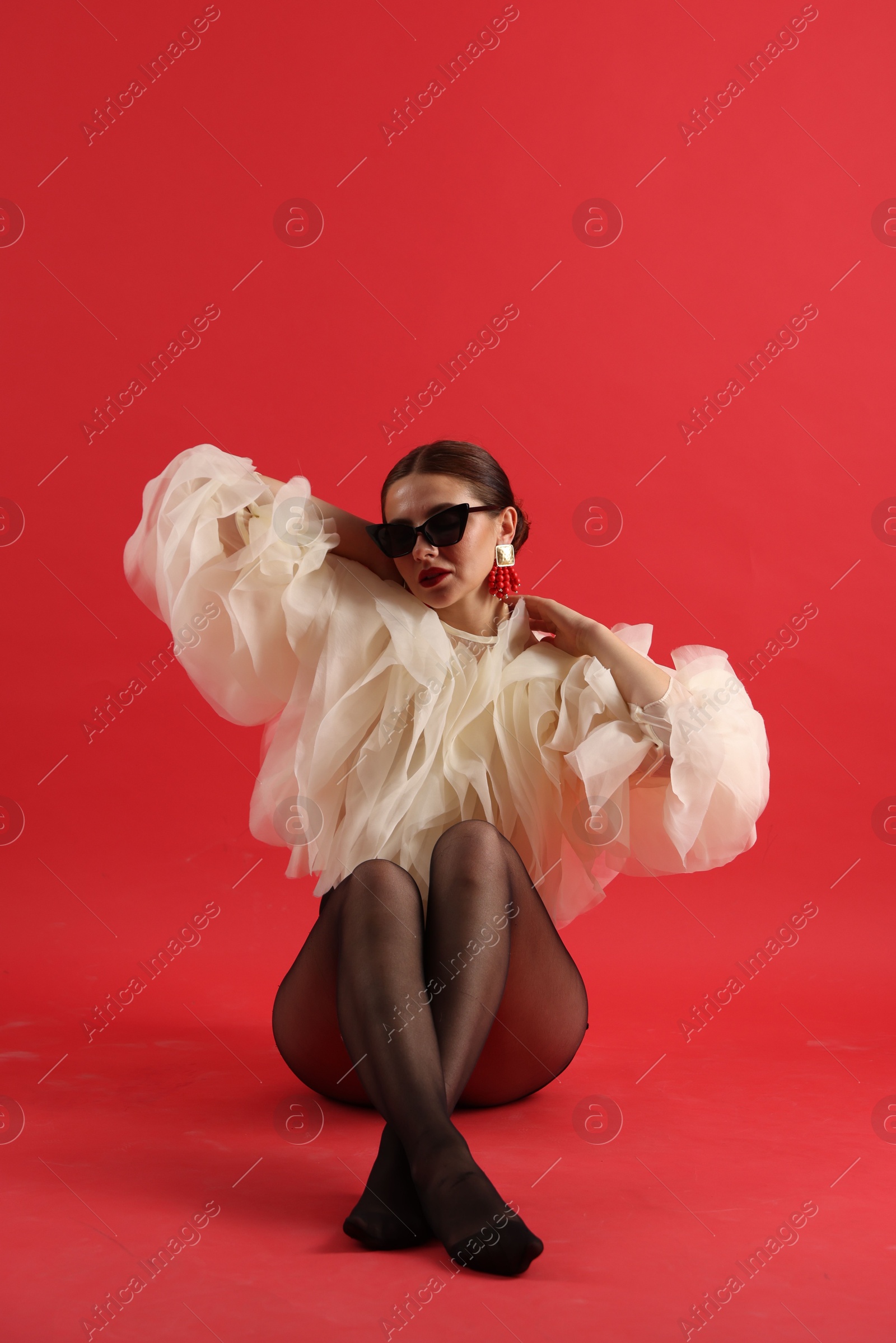 Young woman in stylish clothes and sunglasses on red background Photo of Young woman in stylish clothes and sunglasses on red background