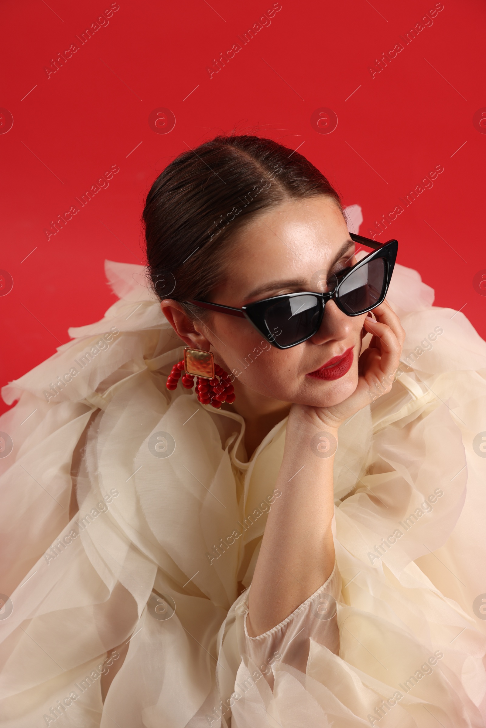 Young woman in stylish clothes and sunglasses on red background Photo of Young woman in stylish clothes and sunglasses on red background