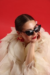 Photo of Young woman in stylish clothes and sunglasses on red background