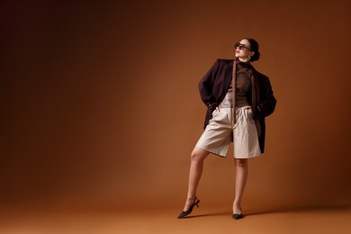 Photo of Young woman in stylish clothes on brown background, space for text