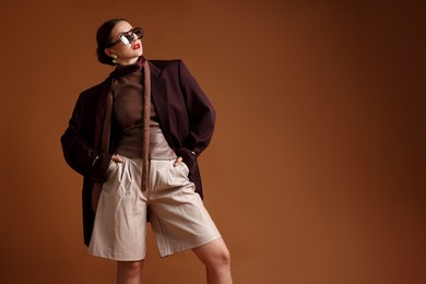 Photo of Young woman in stylish clothes on brown background, space for text