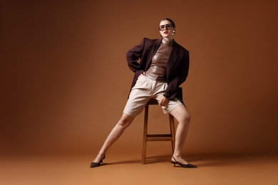 Photo of Young woman in stylish clothes on chair against brown background