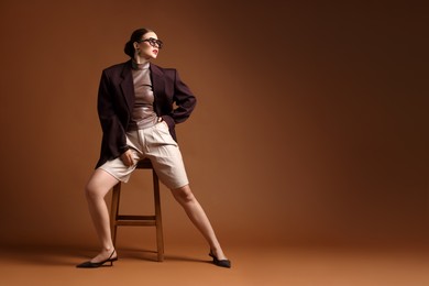 Photo of Young woman in stylish clothes on chair against brown background, space for text