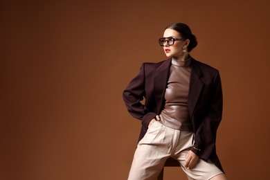Photo of Young woman in stylish clothes on chair against brown background, space for text