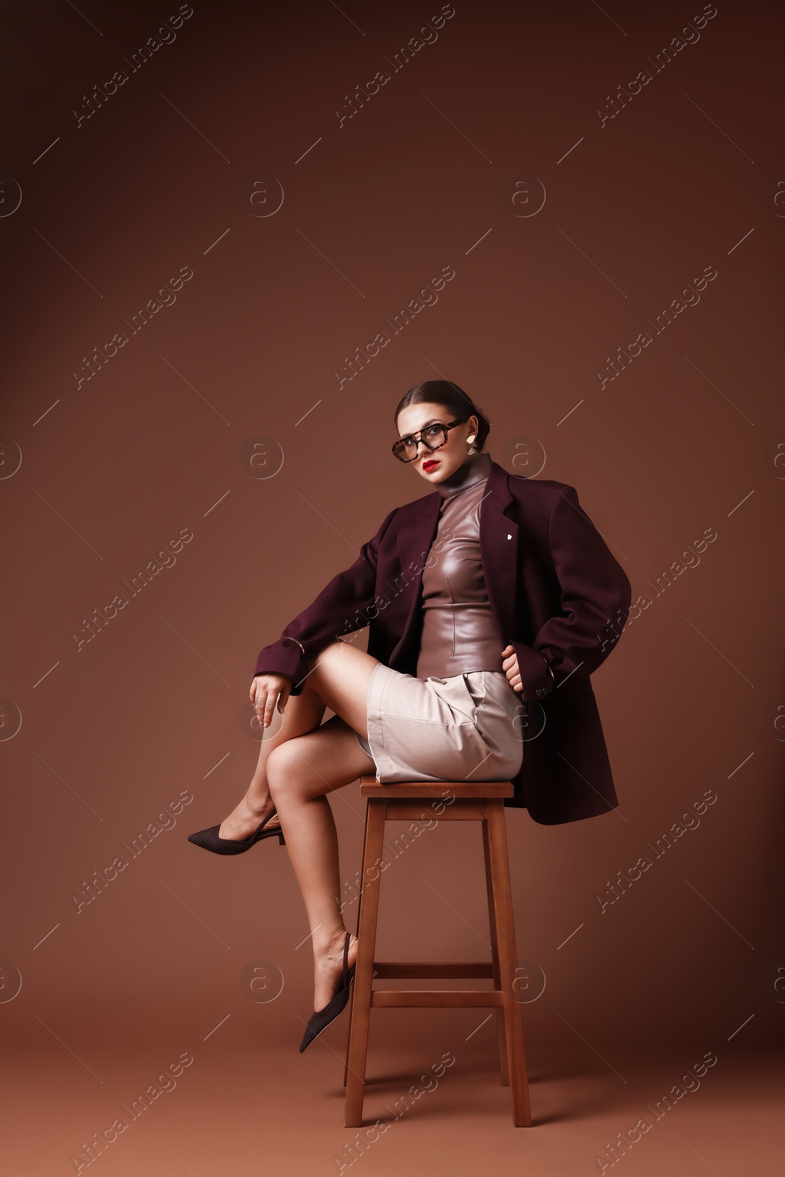 Young woman in stylish clothes on chair against brown background Photo of Young woman in stylish clothes on chair against brown background