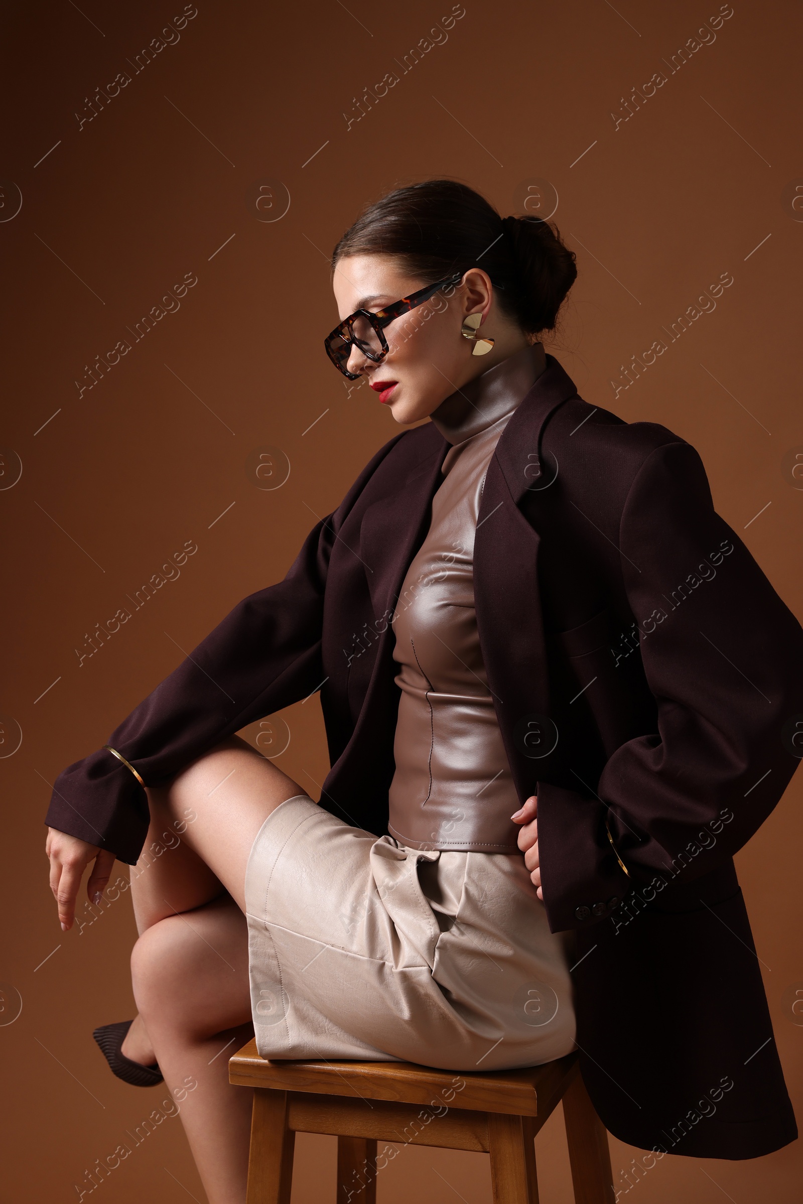 Young woman in stylish clothes on chair against brown background Photo of Young woman in stylish clothes on chair against brown background