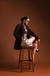 Photo of Young woman in stylish clothes on chair against brown background