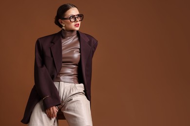 Photo of Young woman in stylish clothes on chair against brown background, space for text