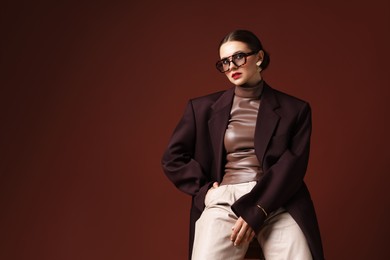 Photo of Young woman in stylish clothes on chair against brown background, space for text