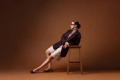 Photo of Young woman in stylish clothes on chair against brown background
