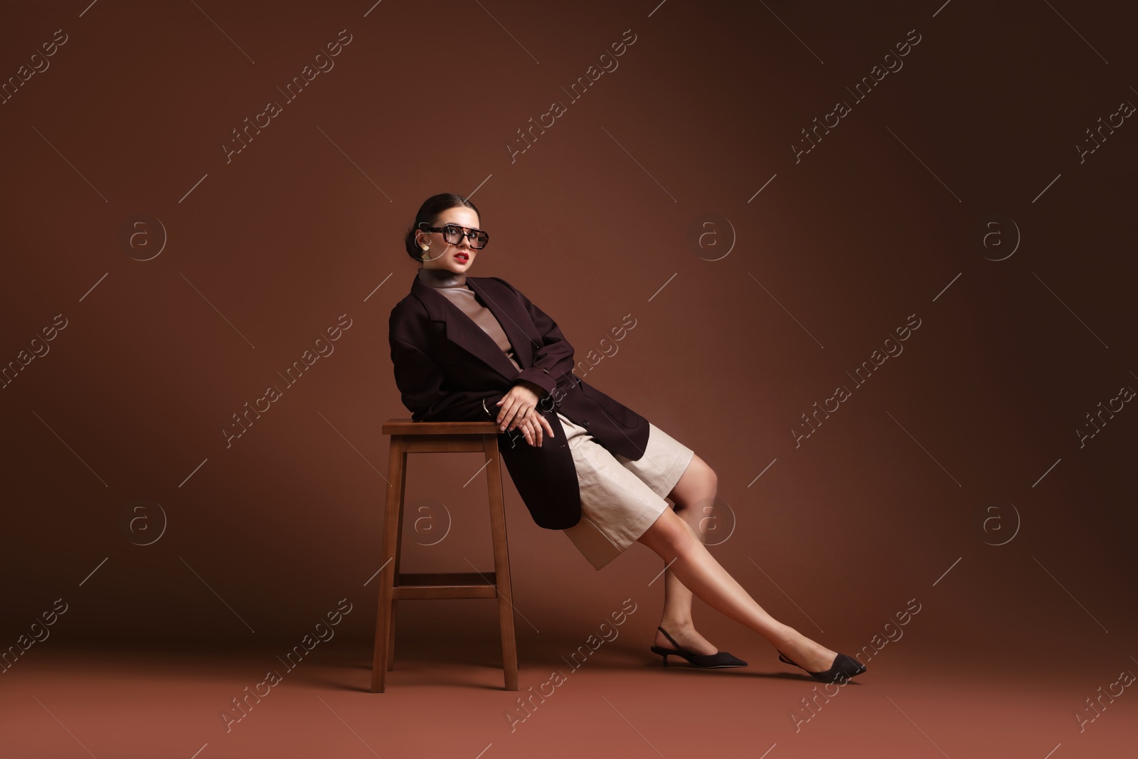 Young woman in stylish clothes on chair against brown background Photo of Young woman in stylish clothes on chair against brown background