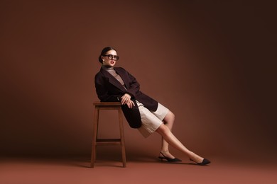 Photo of Young woman in stylish clothes on chair against brown background