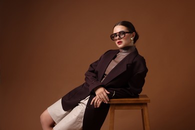 Photo of Young woman in stylish clothes on chair against brown background