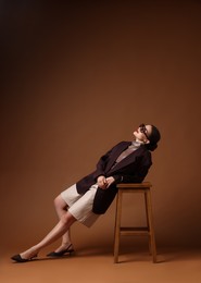 Photo of Young woman in stylish clothes on chair against brown background, space for text