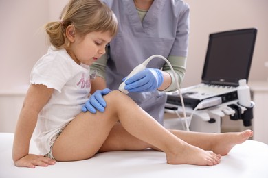 Photo of Sonographer conducting ultrasound examination of little girl's knee in clinic, closeup