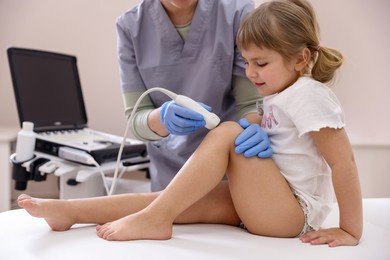 Photo of Sonographer conducting ultrasound examination of little girl's knee in clinic, closeup
