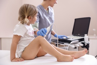 Photo of Sonographer conducting ultrasound examination of little girl's knee in clinic, closeup