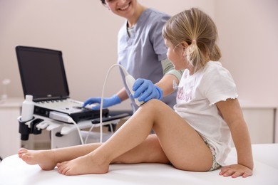 Photo of Sonographer conducting ultrasound examination of little girl's knee in clinic, closeup