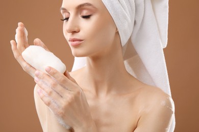 Photo of Beautiful woman with soap bar on brown background, closeup