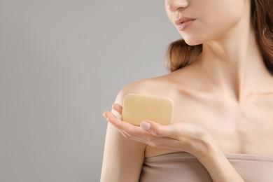 Photo of Woman with soap bar on grey background, closeup. Space for text
