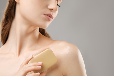 Photo of Woman with soap bar on grey background, closeup. Space for text