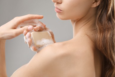 Photo of Woman washing body with soap bar on grey background, closeup