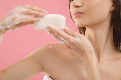 Photo of Woman with foaming soap bar on pink background, closeup