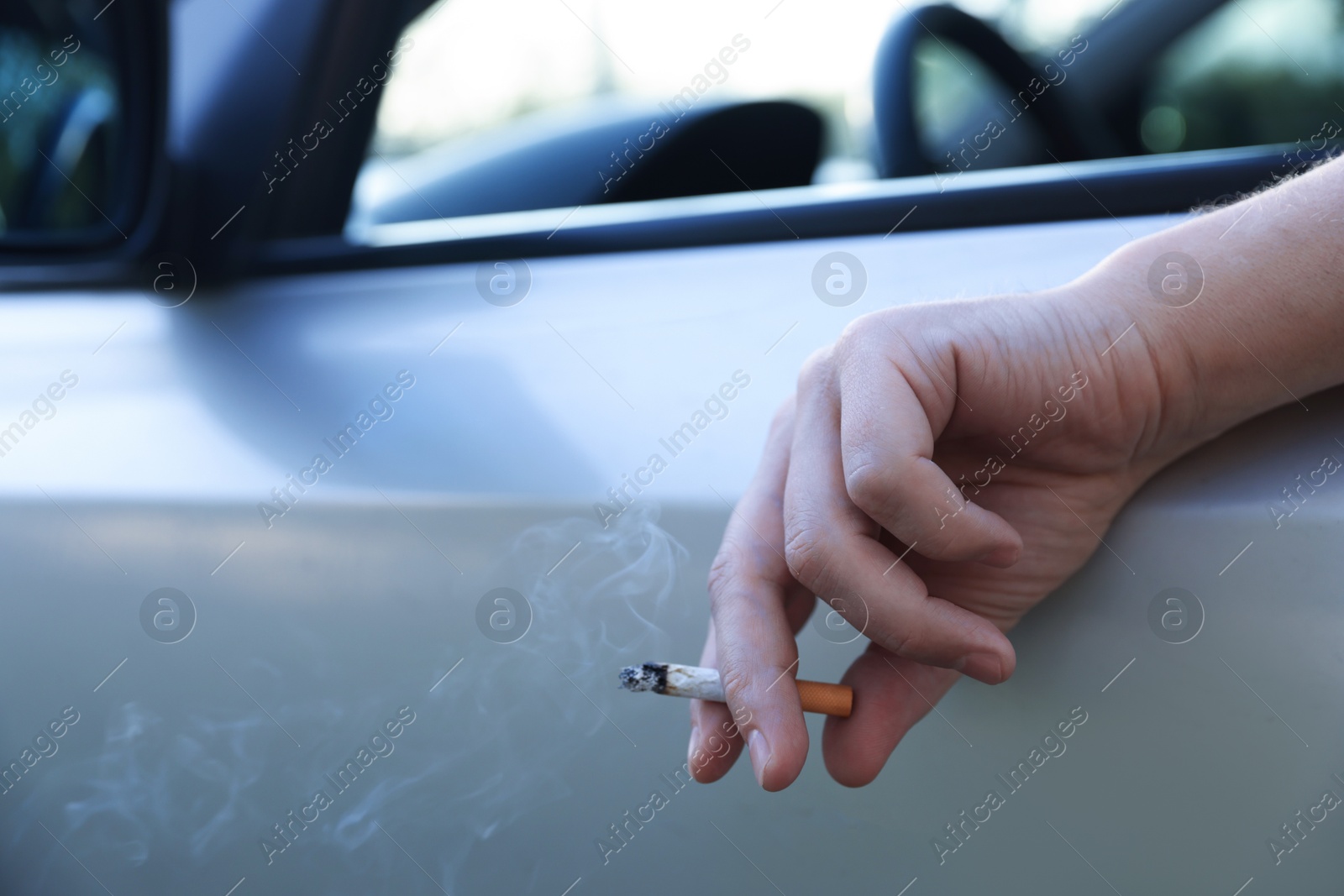 Man smoking while driving in car, focus on cigarette. Space for text Photo of Man smoking while driving in car, focus on cigarette. Space for text