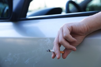 Photo of Man smoking while driving in car, focus on cigarette. Space for text