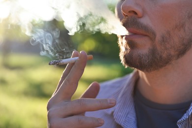 Photo of Man smoking cigarette on blurred background, closeup