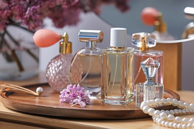 Photo of Bottles of perfumes, accessories and lilac flowers on wooden table, closeup