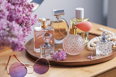 Photo of Bottles of perfumes, accessories and lilac flowers on wooden table