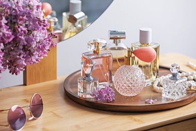 Photo of Bottles of perfumes, accessories and lilac flowers on wooden table
