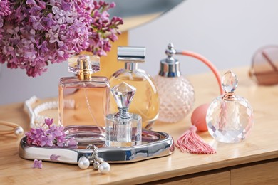 Photo of Bottles of perfumes, accessories and lilac flowers on wooden table